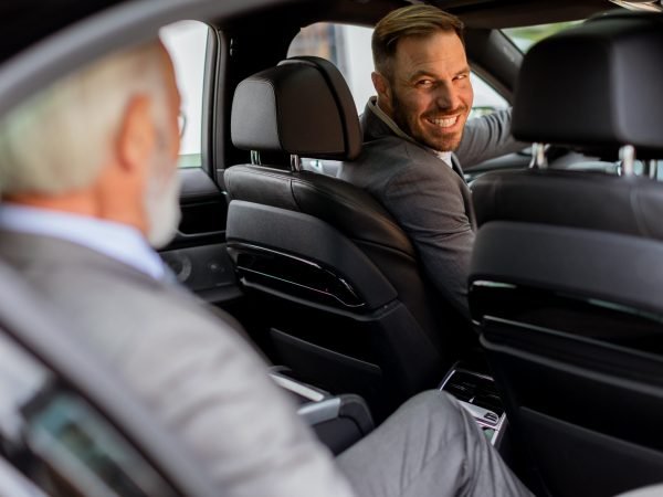 Cheerful man sits in the rear seat of a vehicle, sharing a moment of camaraderie with the driver